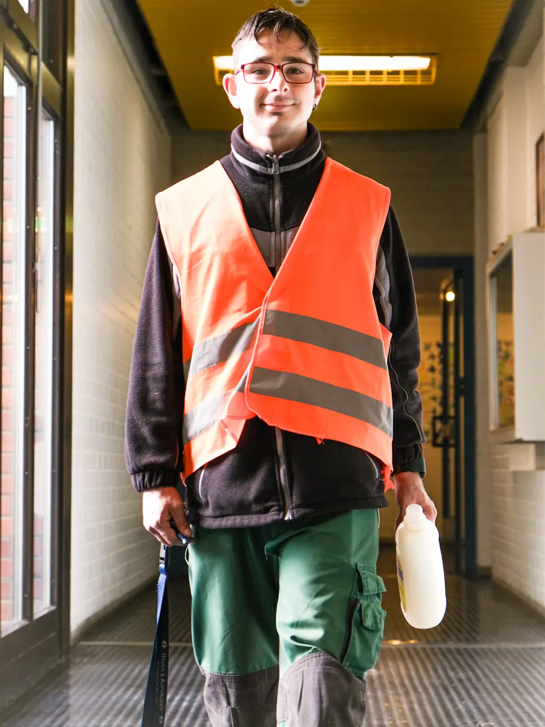 Mann mit Schutzweste und Reinigungsmittel in der Hand in einem Hausflur