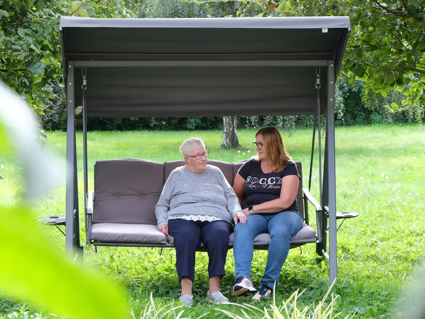 Betreuuerin und Bewohnerin im Garten auf der Hollywoodschaukel