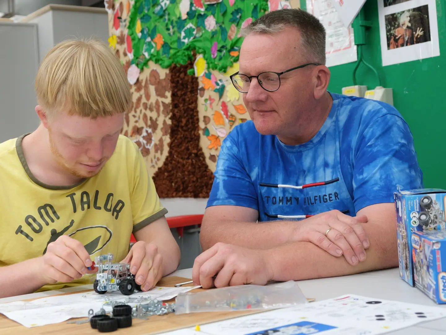 Betreuer und junger Mann arbeiten zusammen an einem technischen Bausatz