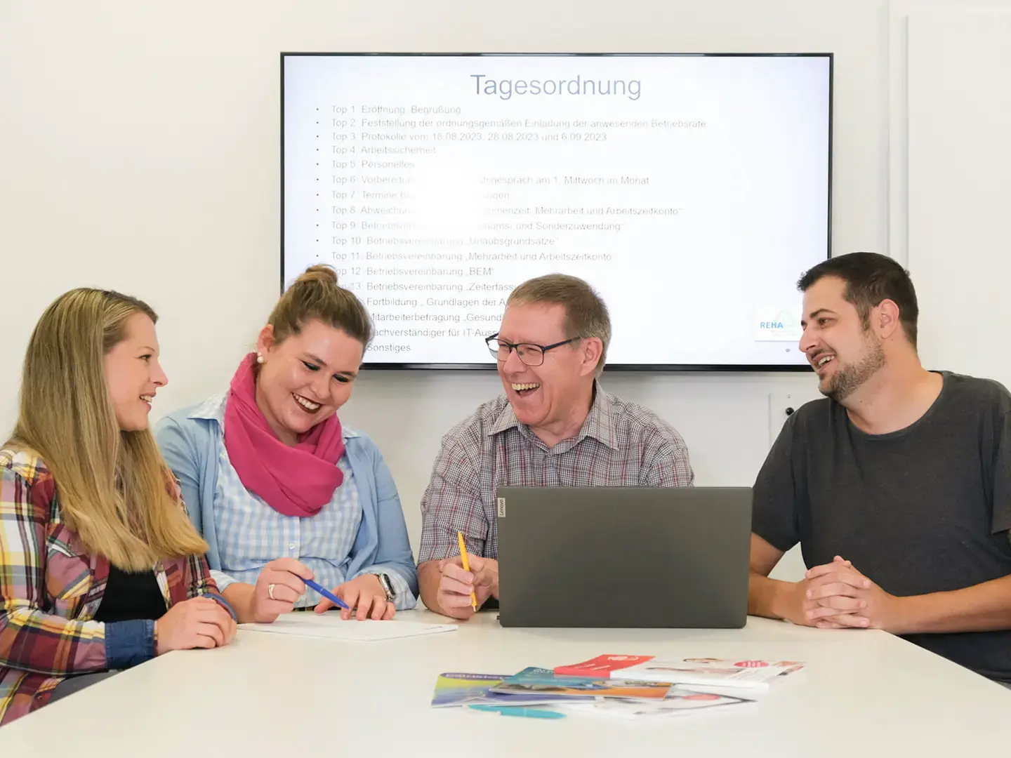 Unser Betriebsrat: zwei Frauen und 2 Männer sitzen im Besprechungsraum und planen am Laptop die nächste Versammlung. Dabei haben sie sichtbar viel Freude.