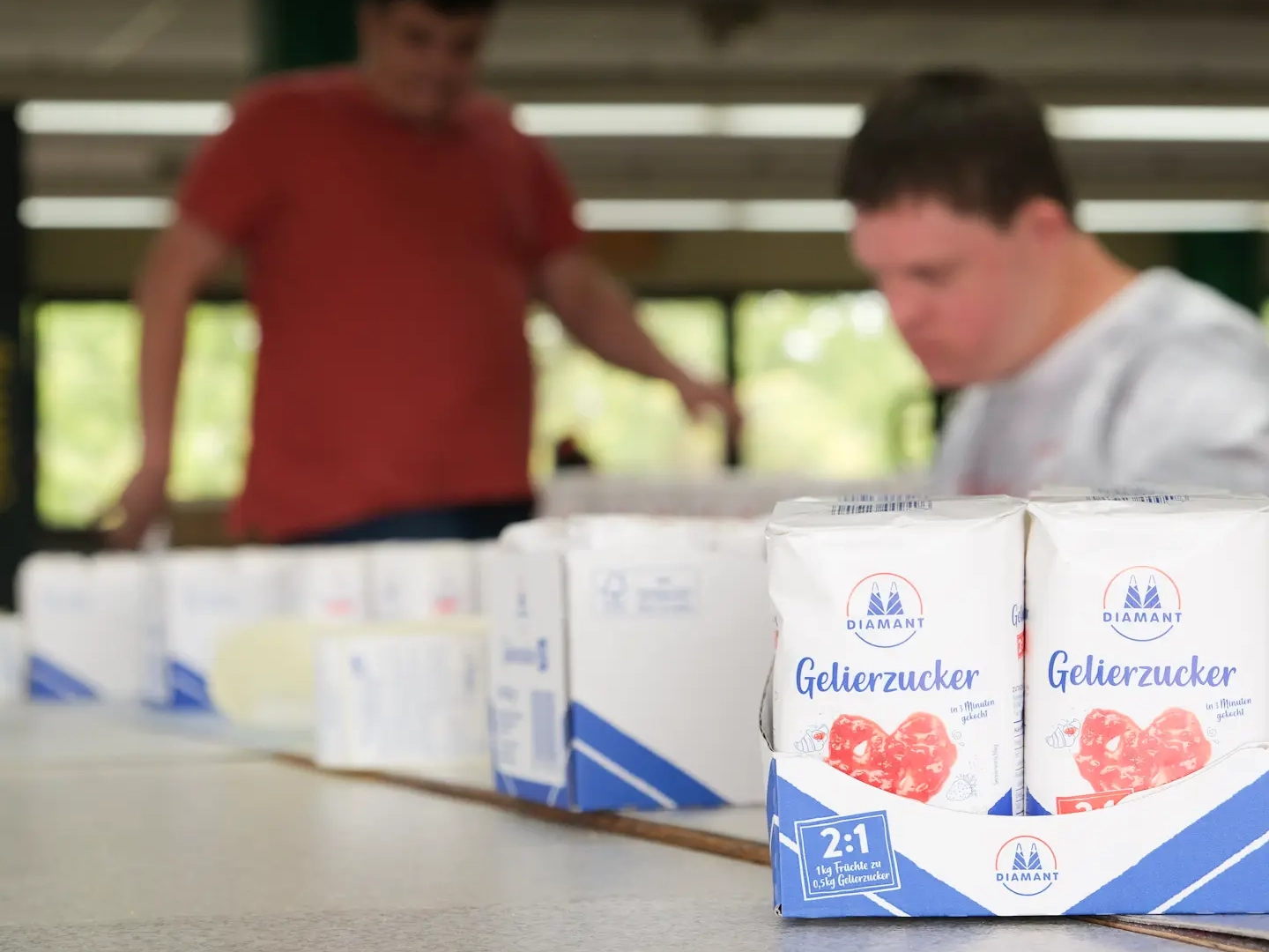 Zwei Werkstattmitarbeiter beim Abpacken von Gelierzuckerpaketen