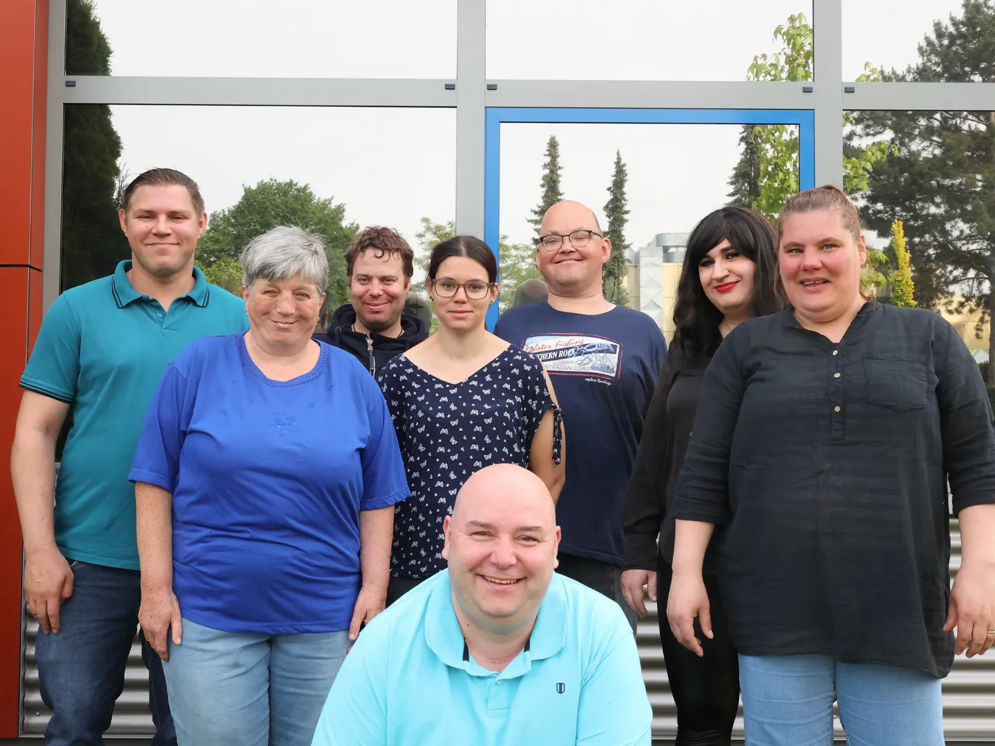 Unser Werkstattrat, 8 Personen, stehen vor dem Gebäude und lächeln fröhlich in die Kamera.