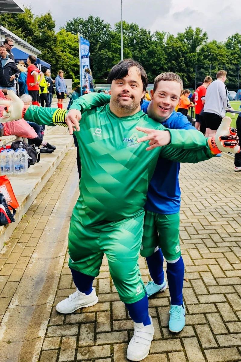 Zwei Spieler der Fußballmannschaft der REHA-Betriebe in ihren neuen Trikots lachen fröhlich in die Kamera.